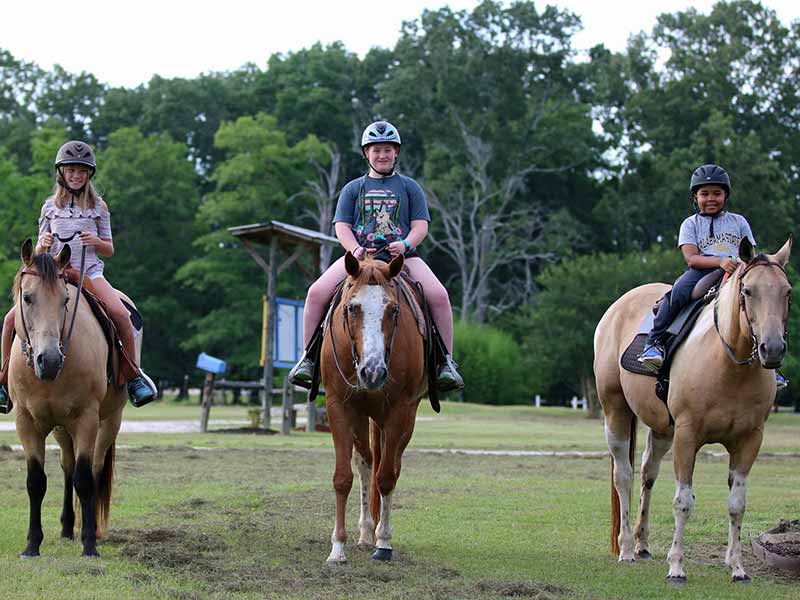Three children in helmets riding horses